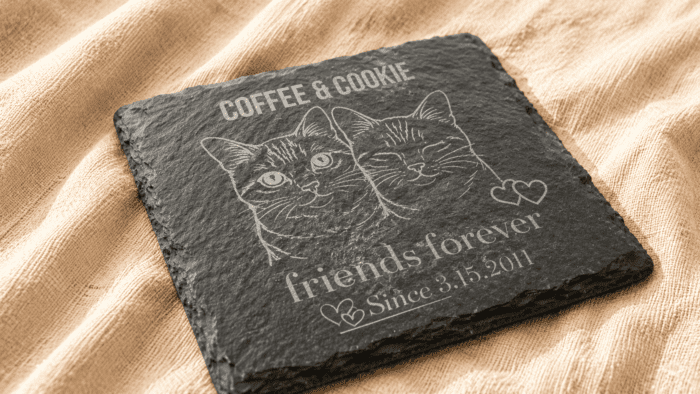Close-Up Personalized Engraved Slate Pet Memorial Coaster Close-up angled view of a personalized engraved square slate pet memorial coaster featuring custom cat portrait artwork and family name engraving on soft cream linen fabric.