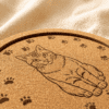 Close-up angled view of a personalized engraved cork pet coaster featuring a custom cat portrait surrounded by paw print details.