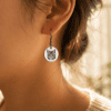 Close-up lifestyle photo of a woman wearing a silver engraved cat portrait earring in warm golden natural light with soft blurred background.