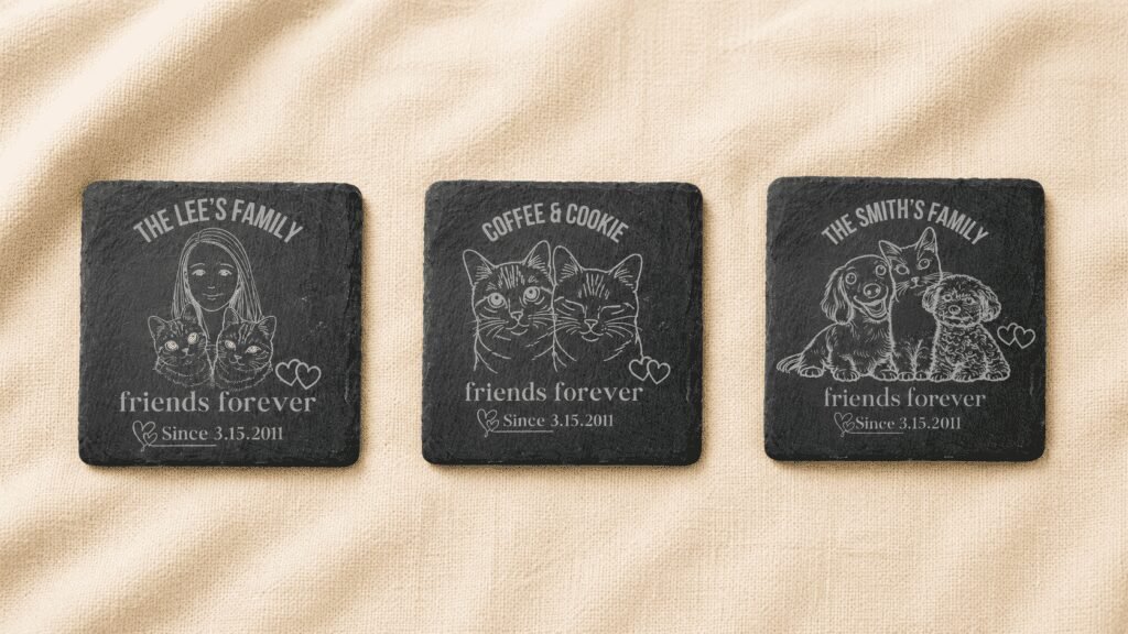 Three personalized engraved slate memorial coasters displayed side by side on cream linen fabric, featuring different family and pet combinations including a woman with two cats, two cats together, and two dogs with a cat.