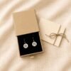 Custom Pet Earrings Gift Packaging Personalized engraved cat portrait earrings presented in a premium kraft gift box with black velvet insert beside a tied thank-you card on cream linen fabric.