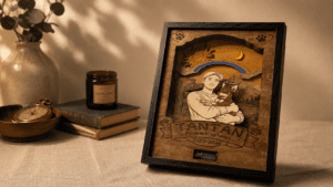 Warm editorial-style photo of a personalized wooden pet memorial shadow box displayed on a linen-covered table beside vintage books, a candle, and soft home décor in golden ambient lighting.