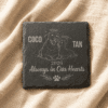 Personalized square slate pet memorial coaster engraved with a dog and cat illustration, resting on soft beige linen fabric.