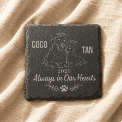 Personalized square slate pet memorial coaster engraved with a dog and cat illustration, resting on soft beige linen fabric.
