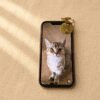 Personalized engraved pet portrait keychain attached to a smartphone displaying the matching cat photo, placed on warm cream linen fabric.