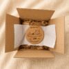 Personalized cork pet memorial coaster packaged inside a kraft shipping box with tissue paper and protective wrapping.