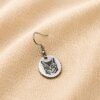 Minimalist Custom Cat Portrait Engraved Earring Close-up product photo of a single silver engraved cat portrait earring resting on soft cream linen fabric with warm natural lighting.