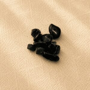 Polished black obsidian crystal chips with a glossy reflective finish arranged on a beige linen fabric background.