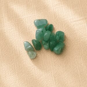 Polished green aventurine crystal chips arranged on a neutral beige linen fabric background with soft natural lighting.