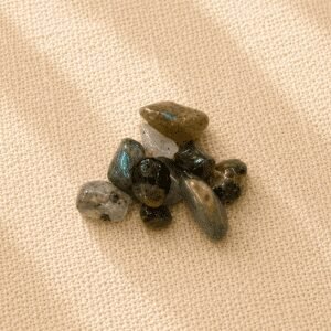 Polished labradorite crystal chips displaying natural flashes of blue, green, and gold on a beige linen fabric background.