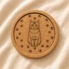 Personalized round cork pet coaster with a custom engraved cat portrait and paw print border displayed on soft neutral linen fabric.