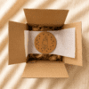 Personalized cork pet coaster packaged inside a kraft gift box with tissue paper and protective wrapping on a soft neutral fabric background.