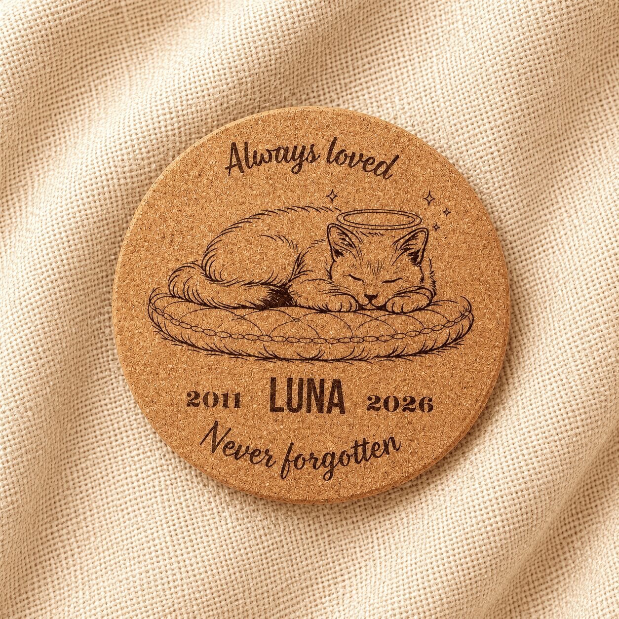 Top-down product photograph of a personalized round cork pet memorial coaster engraved with a sleeping cat illustration, the name Luna, memorial years 2011–2026, and the phrase “Never forgotten,” displayed on soft cream linen fabric.