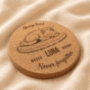 Close-up angled photograph of a personalized round cork pet memorial coaster engraved with a sleeping cat illustration, the name Luna, memorial years 2011–2026, and the phrase “Never forgotten,” displayed on soft neutral linen fabric.