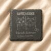 Personalized engraved square slate pet memorial coaster featuring custom cat portrait artwork, family name engraving, and commemorative text displayed on soft cream linen fabric.
