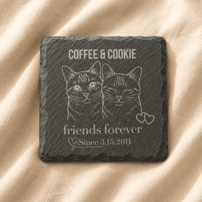 Personalized engraved square slate pet memorial coaster featuring custom cat portrait artwork, family name engraving, and commemorative text displayed on soft cream linen fabric.