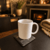 Warm lifestyle photograph of a white mug resting on a personalized slate memorial coaster beside a fireplace in a cozy living room setting.
