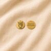 Front and back view of a personalized gold pet memorial charm displayed on cream linen fabric, featuring an engraved cat portrait and the message “Always loved Never forgotten.”