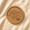 Hero product photo of a personalized engraved cork coaster featuring two cuddling orange tabby cats and the text “Coffee & Cookie,” placed on soft cream linen fabric under warm natural light.