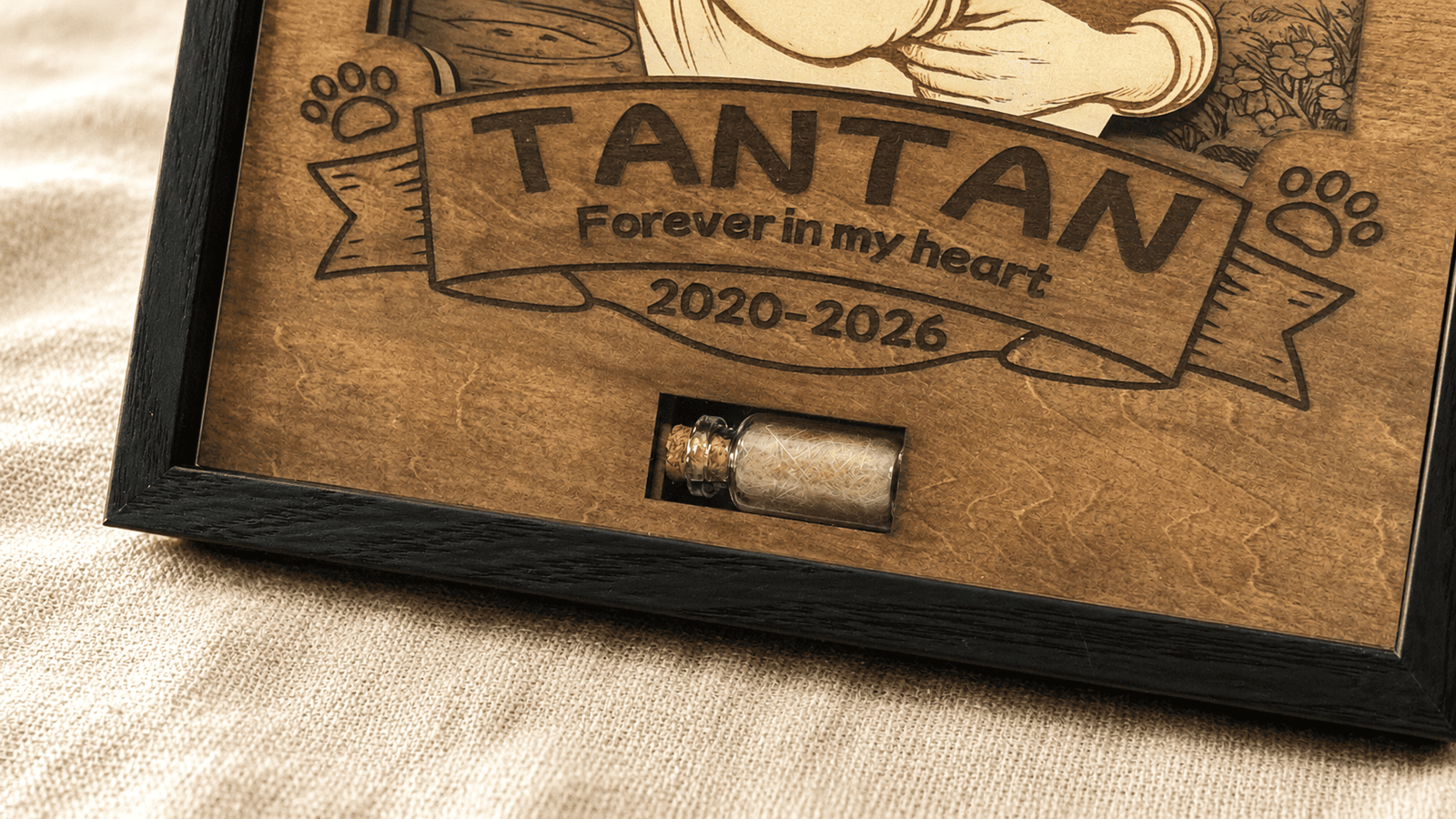 Close-up detail photo of a personalized wooden pet memorial shadow box showing engraved pet name, memorial dates, and a small glass keepsake vial filled with preserved pet fur.