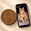 Custom engraved cork pet coaster displayed beside the original cat photo on a smartphone, showing photo-to-engraving personalization process.