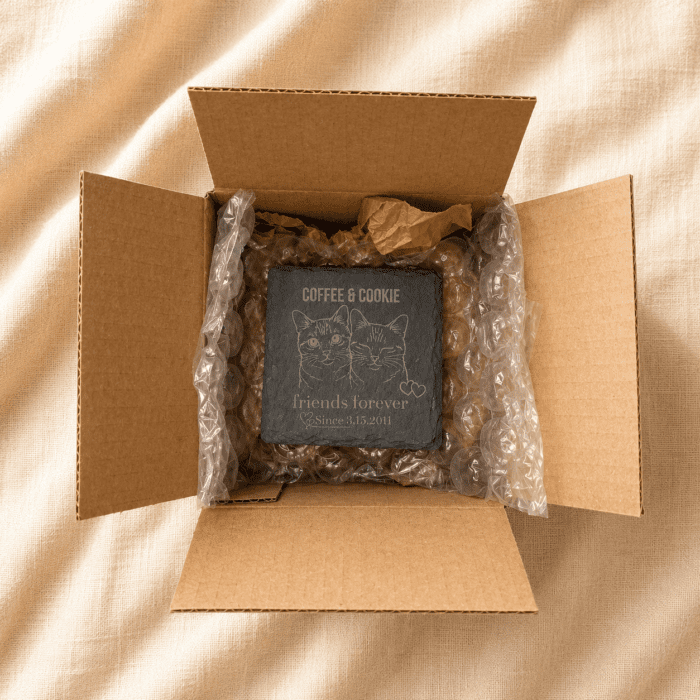 Secure Packaging for Personalized Slate Pet Memorial Coaster Gift Personalized engraved slate pet memorial coaster packaged securely inside a kraft shipping box with protective bubble wrap, displayed on soft cream linen fabric in warm natural lighting.