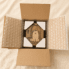 Top-down view of a personalized wooden pet memorial shadow box securely packaged inside a cardboard shipping box with protective corner guards and bubble wrap.