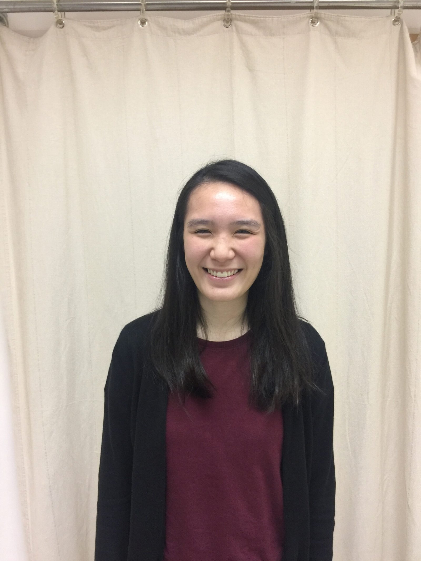Michelle is smiling with long dark hair standing indoors in front of a cream curtain backdrop.