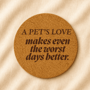 Round cork coaster featuring the engraved quote “A pet’s love makes even the worst days better” in mixed serif and bold italic typography on a warm cream linen background.