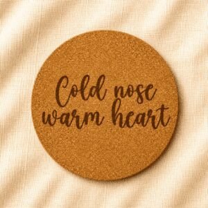 Round cork coaster featuring the engraved quote “Cold nose warm heart” in handwritten script typography on a warm cream linen background.