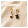Two customizable paw print gemstone earrings displayed on soft cream linen fabric, showing different crystal chip combinations in warm gold-tone settings.
