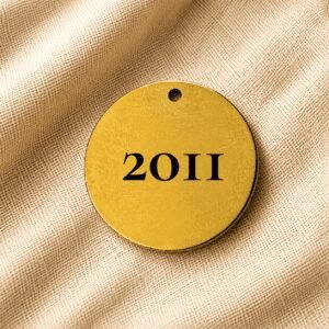 Round gold personalized pet memorial keychain engraved with the year “2011” on a soft beige linen fabric background.