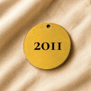 Round gold personalized pet memorial keychain engraved with the year “2011” on a soft beige linen fabric background.