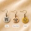 Custom Pet Earrings – Metal Color Options Three personalized engraved pet earrings displayed on beige linen fabric in silver, rose gold, and gold finishes, each featuring a custom pet portrait engraving.