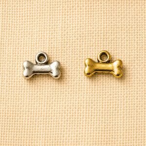 Silver and gold dog bone-shaped memorial charms displayed on a beige linen background, ideal for personalized pet remembrance jewelry, keychains, and keepsakes.