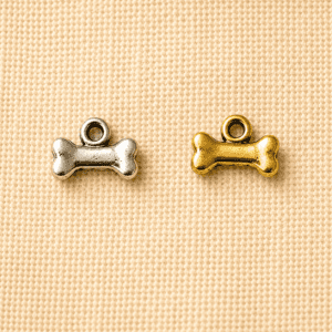 Silver and gold dog bone-shaped memorial charms displayed on a beige linen background, ideal for personalized pet remembrance jewelry, keychains, and keepsakes.