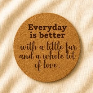 Round cork coaster engraved with the quote “Everyday is better with a little fur and a whole lot of love” in mixed bold and handwritten typography on a soft cream fabric background.