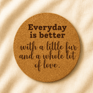 Round cork coaster engraved with the quote “Everyday is better with a little fur and a whole lot of love” in mixed bold and handwritten typography on a soft cream fabric background.