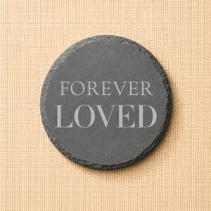 Round slate pet memorial coaster engraved with the words “Forever Loved” on a neutral linen background, a timeless remembrance keepsake for honoring a beloved pet.