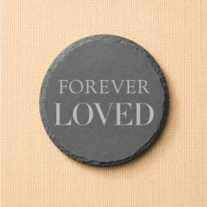 Round slate pet memorial coaster engraved with the words “Forever Loved” on a neutral linen background, a timeless remembrance keepsake for honoring a beloved pet.