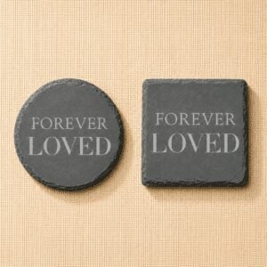 Comparison of round and square slate pet memorial coasters engraved with the phrase “Forever Loved,” displayed side by side on a neutral linen background.