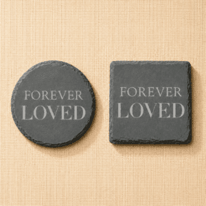Comparison of round and square slate pet memorial coasters engraved with the phrase “Forever Loved,” displayed side by side on a neutral linen background.