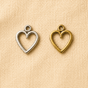 Silver and gold heart-shaped memorial charm pendants displayed on a beige linen background, designed for pet memorial jewelry, keepsakes, and remembrance accessories.