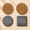 Comparison image showing four memorial coaster material and shape options, including round cork, engraved cork with border, round black slate, and square black slate, displayed on soft cream linen fabric.