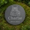Round engraved pet memorial slate displayed outdoors on natural green moss, featuring a detailed cat portrait illustration, the name Charlie, and memorial dates.