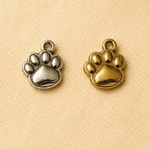 Silver and gold paw print memorial charm pendants displayed on a beige linen background, designed for pet remembrance jewelry, keepsakes, and personalized memorial gifts.