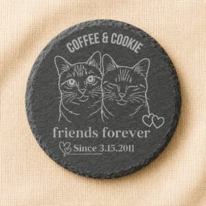 Round black slate coaster engraved with custom portraits of two cats, Coffee and Cookie, featuring the phrase “Friends Forever” and a personalized date, displayed on a warm cream linen background.