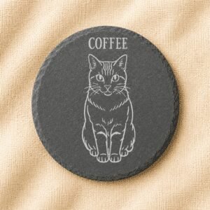 Round black slate coaster with an engraved minimalist portrait of an orange tabby cat named Coffee, displayed on a warm cream linen fabric background.