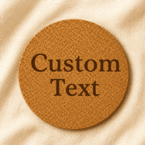 Round cork coaster featuring customizable engraved text in bold serif typography on a natural cork surface with a soft cream linen fabric background.
