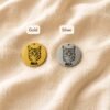 Two personalized pet portrait charms in gold and silver finishes displayed on soft cream linen fabric, each engraved with a cat portrait and the name “MIA.”